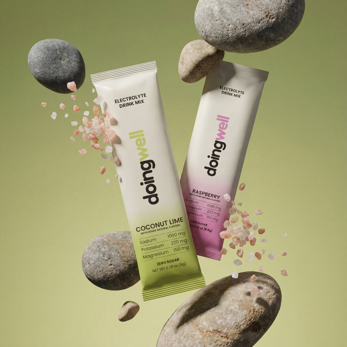 Alt text: DoingWell Coconut Lime and Raspberry stick packs floating in a balanced composition with smooth gray river stones and scattered Himalayan pink salt crystals, against a soft sage green background, both cream-to-green and cream-to-pink gradient packaging visible with doingwell logo and electrolyte stats